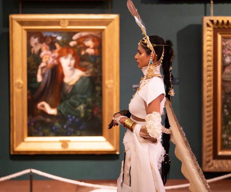 Model in an elaborate white and gold outfit poses beside a classical painting in an ornate gold frame at Fashion Frenzee by Central London Alliance, part of London Fashion Week, inside Guildhall Art Gallery