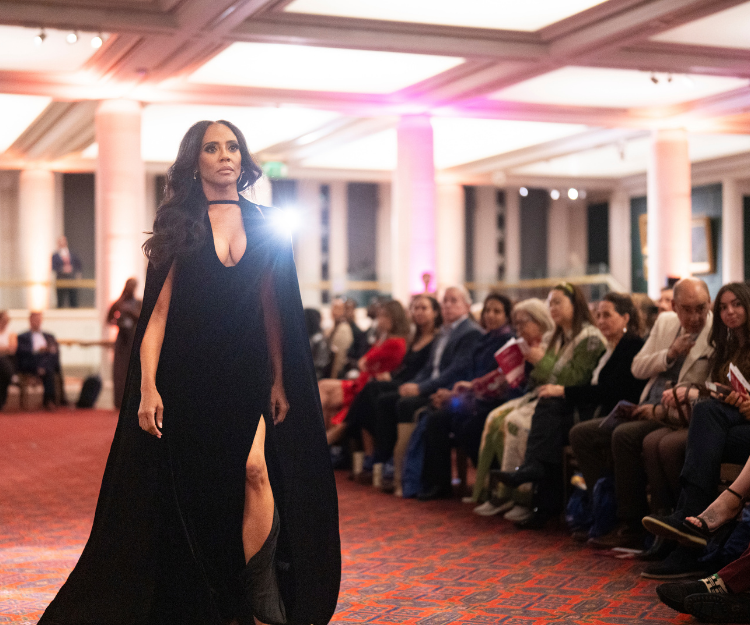 Female model wears a plunging black evening gown with a thigh-high slit, walking the runway at Fashion Frenzee by Central London Alliance, part of London Fashion Week